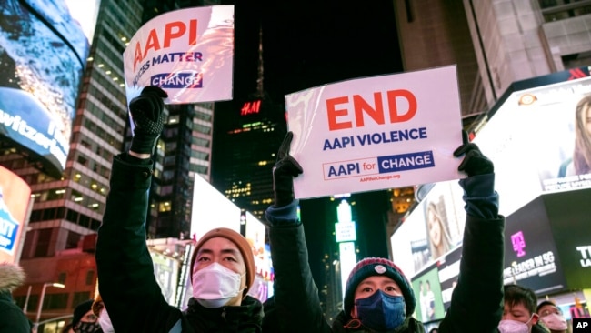 People hold signs in support of Asian American Pacific Islander communities while attending a candlelight vigil in honor of Michelle Alyssa Go, a victim of a recent subway attack, at Times Square on Jan. 18, 2022, in New York.