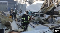 Rescue workers walk past debris and cars under ruins in front of the shopping and entertainment center in the Ukrainian Black Sea city of Odessa on May 10, 2022, destroyed after Russian missiles strike late on May 9, 2022.