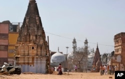 In this March 19, 2019, photo, 17th-century Gyanvapi mosque, white structure sandwiched between Hindu temples, is seen in the background as Hindu devotees walk at the site of a proposed grand promenade connecting the sacred Ganges river with a centuries-old temple dedicated to Lord Shiva, in Varanasi, India. (AP Photo/Altaf Qadri)