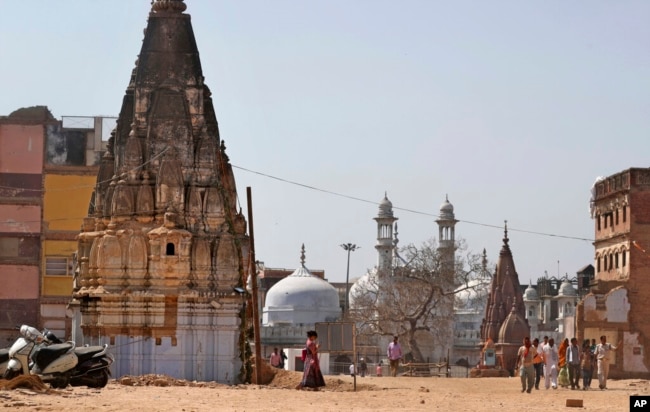 In this March 19, 2019, photo, 17th-century Gyanvapi mosque, white structure sandwiched between Hindu temples, is seen in the background as Hindu devotees walk at the site of a proposed grand promenade connecting the sacred Ganges river with a centuries-old temple dedicated to Lord Shiva, in Varanasi, India. (AP Photo/Altaf Qadri)