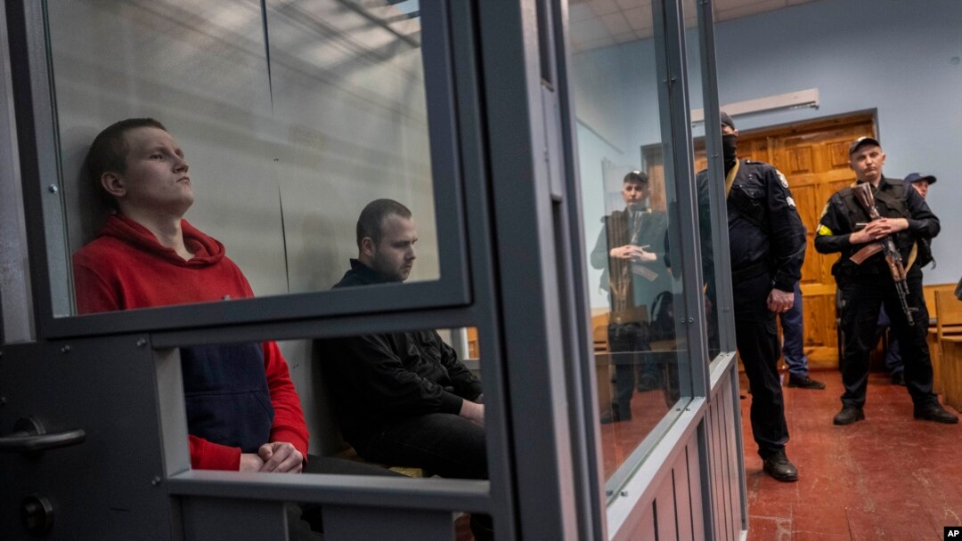 Russian soldiers Alexander Ivanov, right, and Alexander Bobikin sit in a glass box at their trial in Kotelva, northeastern Ukraine, May 26, 2022.