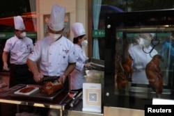 Staff members prepare roast duck for take-away orders during lunch hours at a stall set up outside a restaurant in Beijing May 17, 2022. (REUTERS/Tingshu Wang)