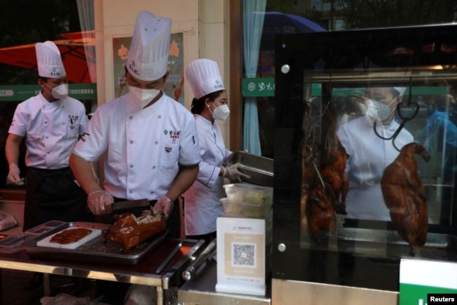 Staff members prepare roast duck for take-away orders during lunch hours at a stall set up outside a restaurant in Beijing May 17, 2022. (REUTERS/Tingshu Wang)