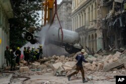Bomberos rocían con agua un camión cisterna de gas para enfriarlo al removerlo del lugar de la explosión en el Hotel Saratoga de La Habana el 6 de mayo de 2022.