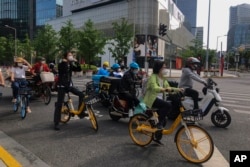 上海市民和快递小哥骑着车在街头等交通灯。（2022年5月31日）