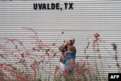 FILE - A woman cries and hugs a young girl while on the phone outside the Willie de Leon Civic Center Uvalde, Texas, on May 24, 2022.