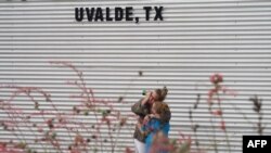 A woman cries and hugs a young girl while on the phone outside the Willie de Leon Civic Center in Uvalde, Texas, on May 24, 2022, the day of a mass shooting at an elementary school in Uvalde, Texas.