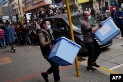 FILE - A Hong Kong National Security police officer, center, and a worker carry boxes of evidence from the offices of Stand News in Hong Kong, Dec. 29, 2021.