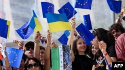 People wave Ukrainian and European flags during an Europe Day Ceremony in support of Ukraine hosted near the headquarters of the European Commission in Brussels on May 9, 2022.