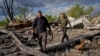 Villagers walk past unexploded artillery shells as they collect scrap metal from a bombed warehouse in the village of Malaya Rohan, Kharkiv region, May 18, 2022. 