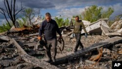 Villagers walk past unexploded artillery shells as they collect scrap metal from a bombed warehouse in the village of Malaya Rohan, Kharkiv region, May 18, 2022. 