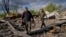 Villagers walk past unexploded artillery shells as they collect scrap metal from a bombed warehouse in the village of Malaya Rohan, Kharkiv region, May 18, 2022. 