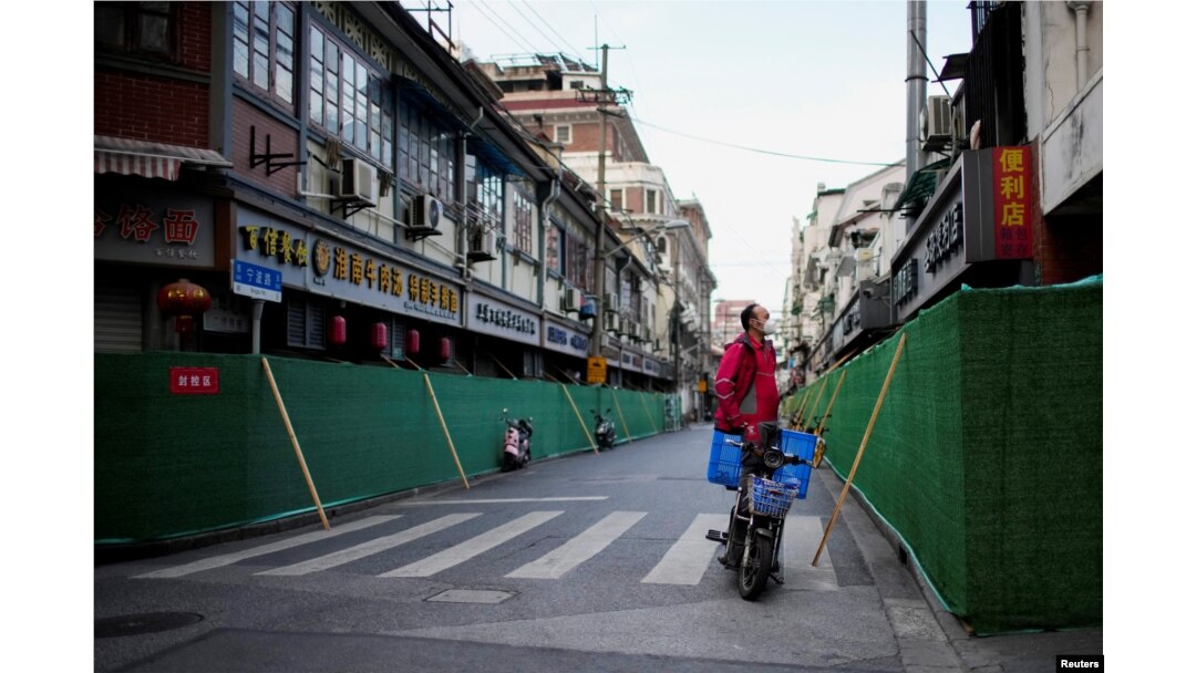 Seorang pekerja pengiriman berdiri di atas skuter melihat melewati penghalang di area perumahan tertutup selama penguncian, di tengah pandemi COVID-19, di Shanghai, China, 9 Mei 2022. (Foto: REUTERS/Aly Song)