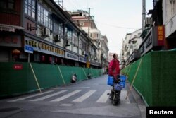 Seorang pekerja pengiriman berdiri di atas skuter melihat melewati penghalang di area perumahan tertutup selama penguncian, di tengah pandemi COVID-19, di Shanghai, China, 9 Mei 2022. (Foto: REUTERS/Aly Song)