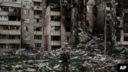 Ukraynalı hərbçi Xarkiv şəhərində cəbhə xətti yaxınlığında Rusiyanın çoxsaylı bombardmanları nəticəsində ciddi ziyan dəymiş binanın dağıntıları arasında gəzir, 25 aprel 2022-ci il.