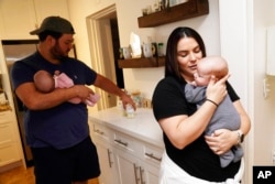 Lisette Fernandez holds newborn son Luca as her husband George holds daughter Lexi while also getting their bottles ready, in Coral Gables, Fla., May 24, 2022.