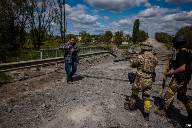 Soldiers of the Kraken Ukrainian special forces unit check a man's documents at a destroyed bridge on the road near the village of Rus'ka Lozova, north of Kharkiv, on May 16, 2022. (Photo by Dimitar DILKOFF / AFP)