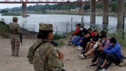 Migrantes que cruzaron el río Bravo hacia EEUU están bajo la custodia de miembros de la Guardia Nacional mientras esperan la llegada de los agentes de la Patrulla Fronteriza EEUU en Eagle Pass, Texas, el viernes 20 de mayo de 2022.