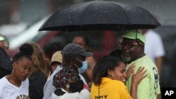 Bystanders gather under an umbrella as the rain rolls after shooting at a supermarket on May 14, 2022 in Buffalo, NY