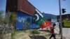 A supporter of Pakistan's Tehreek-e-Insaf (PTI) party carries flags next to containers stacked by authorities to block the Red Zone ahead of a planned rally in support of former Prime Minister Imran Khan, in Islamabad, May 24, 2022.