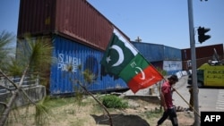 A supporter of Pakistan's Tehreek-e-Insaf (PTI) party carries flags next to containers stacked by authorities to block the Red Zone ahead of a planned rally in support of former Prime Minister Imran Khan, in Islamabad, May 24, 2022.