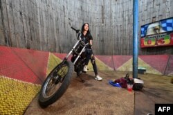 FILE - Daredevil Karmila Purba, a rider of the "wall of death," sits on her bike before a performance inside a six-meter-high wall at a night carnival in Bogor, Indonesia, April 30, 2022.