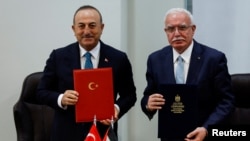 FILE - Turkish Foreign Minister Mevlut Cavusoglu and Palestinian Foreign Minister Riyad al-Maliki hold documents as they sign agreements during a meeting, in Ramallah, in the Israeli-occupied West Bank, May 24, 2022. 