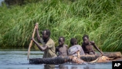 FILE - A father and his sons transport cows from a flooded area to drier ground using a dugout canoe, in Old Fangak county, Jonglei state, South Sudan on Nov. 25, 2020.