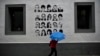 Seoraang perempuan berjalan dengan payung melewati dinding sebuah bangunan di mana sejumlah gambar dari tahanan kelompok separatis Basque (ETA) tersemat pada bangunan tersebut yang terletak di Desa Hernani, wilayah utara Spanyol, pada 2 Mei 2018. (Foto: AP/Alvaro Barrientos)