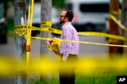 A person brings flowers to the perimeter of the scene of a shooting at a supermarket, in Buffalo, N.Y., May 16, 2022.