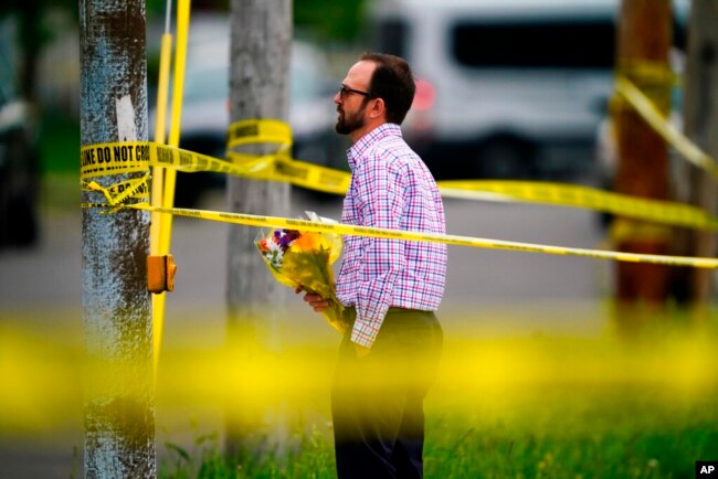 A person brings flowers to the perimeter of the scene of a shooting at a supermarket, in Buffalo, N.Y., May 16, 2022.