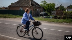 Social worker Zhanna Protsenko, 56, rides her bicycle in front of a house damaged by shelling in the town of Orikhiv, near Zaporizhzhia, eastern Ukraine, on May 11, 2022.