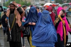 Wanita Afghanistan berjalan melalui pasar lama saat seorang pasukan Taliban berjaga-jaga, di pusat kota Kabul, Afghanistan, Selasa, 3 Mei 2022. (Foto: AP)