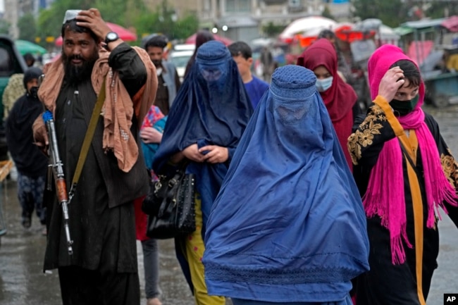 Wanita Afghanistan berjalan melalui pasar lama saat seorang pasukan Taliban berjaga-jaga, di pusat kota Kabul, Afghanistan, Selasa, 3 Mei 2022. (Foto: AP)