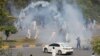 Supporters of the Pakistan Tehreek-e-Insaf (PTI) political party run with batons amid the tear gas smoke fired by police to prevent them from attending a protest march to Islamabad, in Rawalpindi, Pakistan, May 25, 2022.