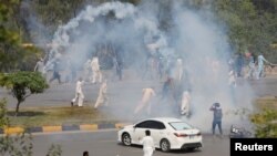 Supporters of the Pakistan Tehreek-e-Insaf (PTI) political party run with batons amid the tear gas smoke fired by police to prevent them from attending a protest march to Islamabad, in Rawalpindi, Pakistan, May 25, 2022.