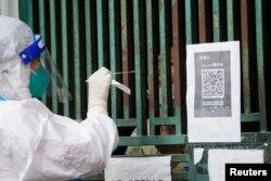 Seorang pekerja medis dengan pakaian pelindung mengambil sampel swab dari seorang warga untuk pengujian asam nukleat, di luar pintu masuk tertutup sebuah gedung saat lockdown, di tengah pandemi COVID-19, di Shanghai, China, 5 Mei 2022. (Foto: REUTERS/ Lagu Ali)