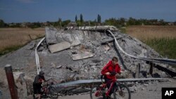 Teenagers on bicycles pass a bridge destroyed by shelling near Orihiv, Ukraine, May 5, 2022.