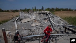 Teenagers on bicycles pass a bridge destroyed by shelling near Orihiv, Ukraine, May 5, 2022.
