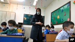 A teacher helps her students as they wear face masks to help prevent the spread of the coronavirus in their elementary school in Tehran, Iran, April 11, 2022. 