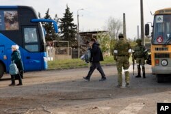 Los residentes locales que abandonaron un refugio en el Combinado Metalúrgico Azovstal caminan hacia un autobús escoltado por militares del ejército ruso y la milicia de la República Popular de Donetsk en Mariúpol, en territorio bajo el gobierno de la República Popular de Donetsk, en el este de Ucrania, el viernes 6 de mayo de 2022. (Foto AP/Alexei Alexandrov)