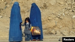 FILE - Afghan women clad in burkas wait for transportation on a road in Kabul, Nov. 5, 2012.