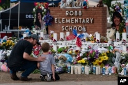 A man and a boy visit a memorial at Robb Elementary School in Uvalde, Texas, May 29, 2022, to pay their respects for the victims killed in a school shooting.