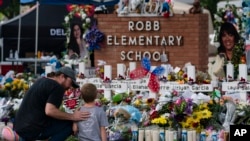 A man and a boy visit a memorial at Robb Elementary School in Uvalde, Texas, May 29, 2022, to pay their respects for the victims killed in a school shooting. 