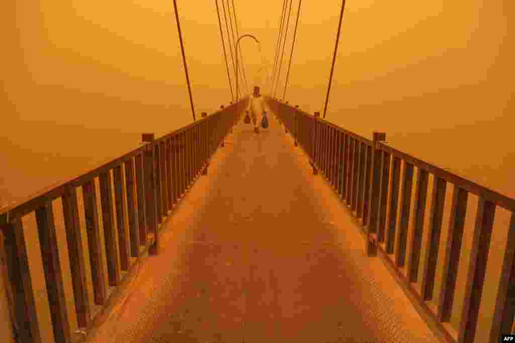A man walks on a pedestrian bridge along the Euphrates river in the city of Nasiriyah in Iraq's southern Dhi Qar province, May 16, 2022 amidst a heavy dust storm. 