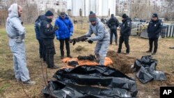FILE - French forensics investigators, who arrived to Ukraine to investigate war crimes amid Russia's invasion, stand next to a mass grave in the town of Bucha, in Kyiv region, Ukraine, April 12, 2022.
