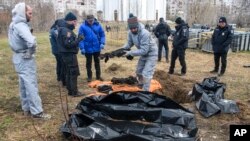 FILE - French forensics investigators, who arrived to Ukraine to investigate war crimes amid Russia's invasion, stand next to a mass grave in the town of Bucha, in Kyiv region, Ukraine, April 12, 2022.
