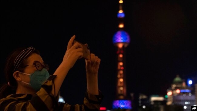 A woman takes photos near the Oriental Pearl Tower on the bund, Tuesday, May 31, 2022, in Shanghai. (AP Photo/Ng Han Guan)