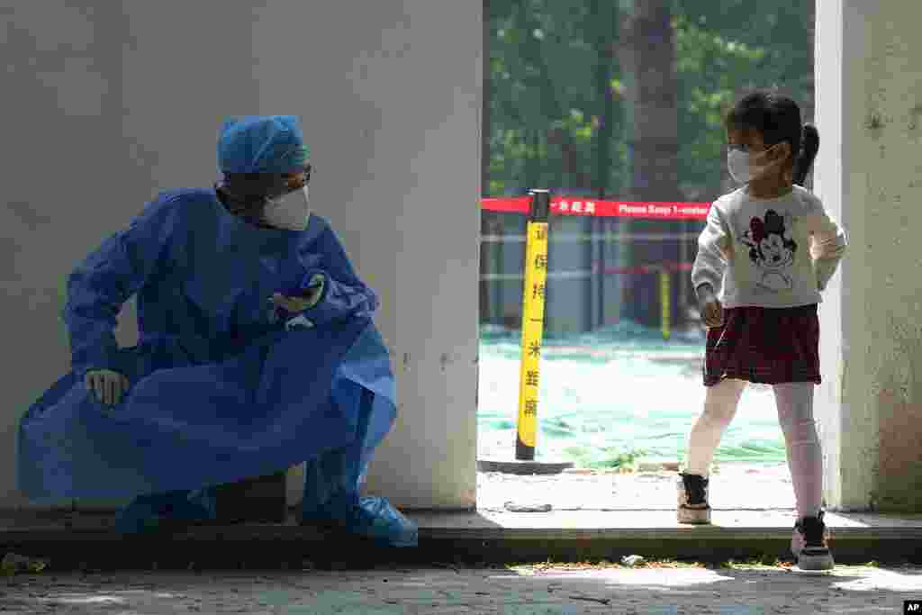 A worker in protective gear looks at a child leaving after mass COVID test in Beijing.