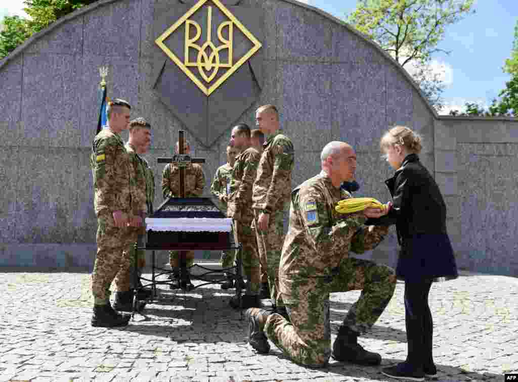 A serviceman offers the Ukrainian flag to the daughter of Yuriy Huk, a Ukrainian serviceman, killed during the Russian invasion of Ukraine, at his funeral service at the Saints Peter and Paul Garrison Church, in the western Ukrainian city of Lviv, May 16,